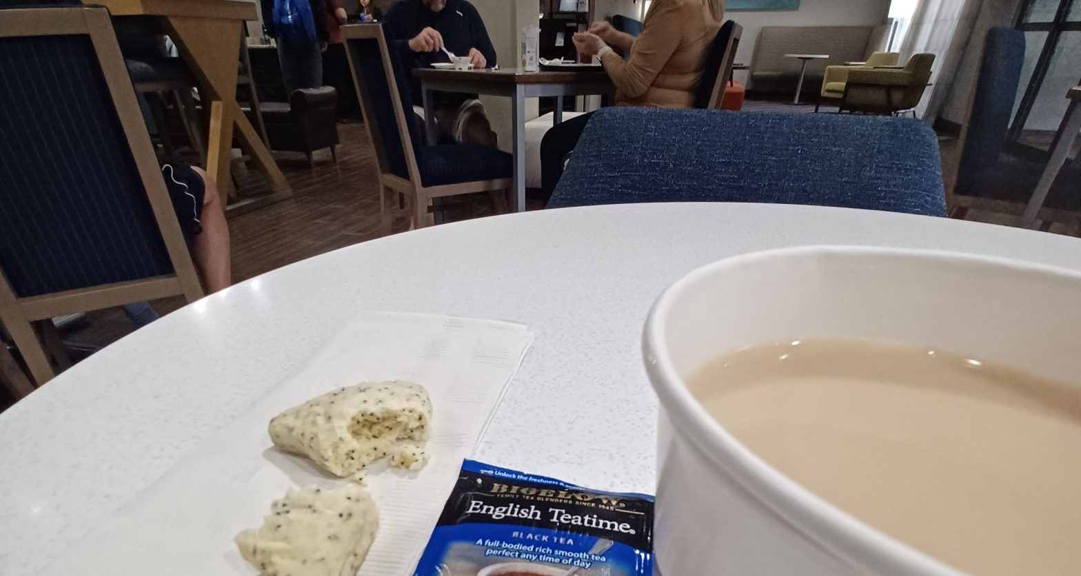 A paper cup with tea on a table in a hotel breakfast room.